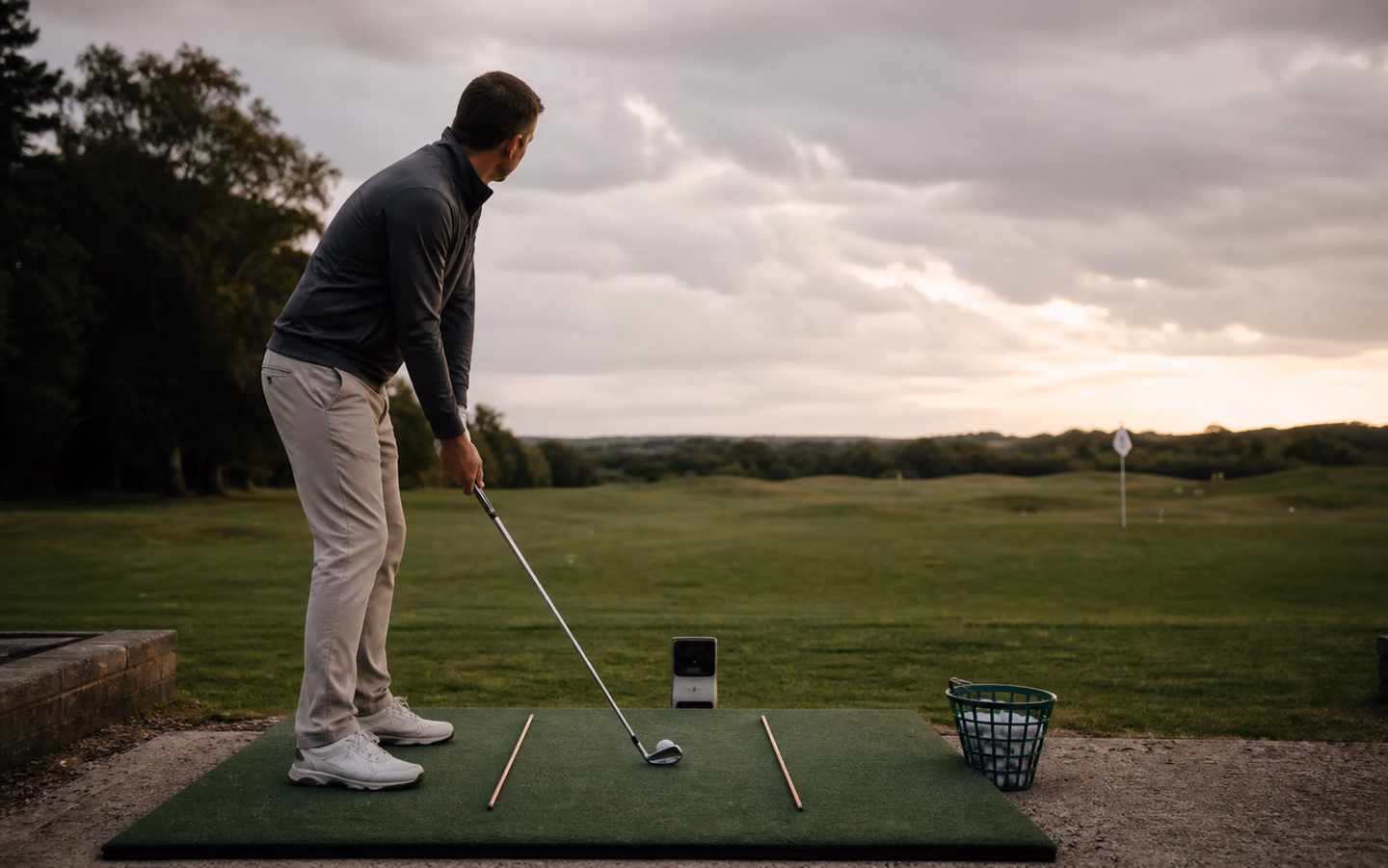 Golfer setting up a measured range practice station with alignment rods and a launch monitor